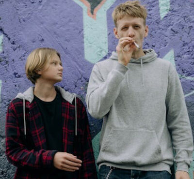 Two young men stand side by side, smoke